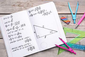 Copybook with maths formulas and stationery on grey wooden background