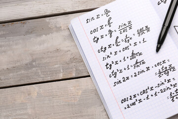 Copybook with maths formulas and pen on grey wooden background