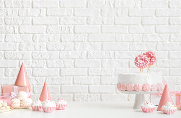 Birthday cake with sweets on white table near brick wall