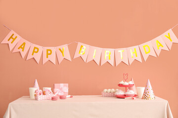 Sweets on white table and happy birthday paper garlands on dark beige wall