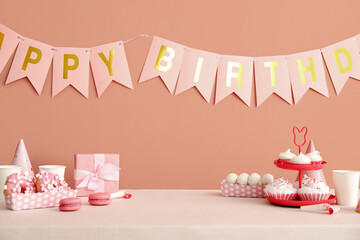 Sweets on white table and happy birthday paper garlands on dark beige wall
