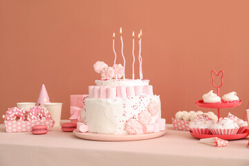 Birthday cake with candles and sweets on white table near dark beige wall