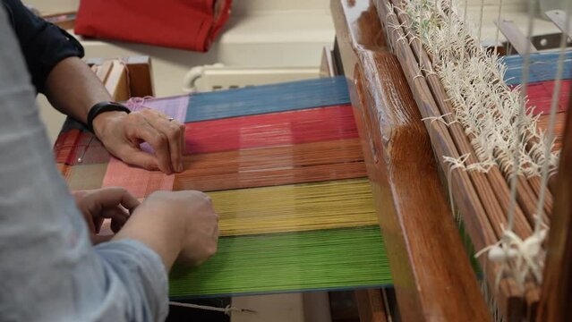  Textile industry, Woman hand working with weaving loom at textile factory. Closeup of woman weaver producing fabric on weaving machine. Process of material production. Textile industry manufacturing