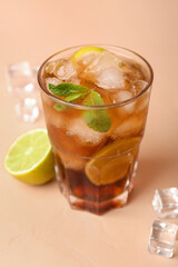 Glass of cold Cuba Libre cocktail on beige background