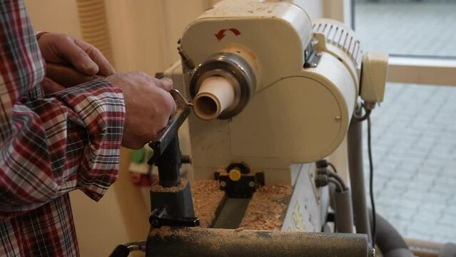 Man carpenter using chisel for shaping piece of wood on turning lathe machine with many shavings at workshop - close up. Carpentry, hobby, craftsmanship and woodworking concept