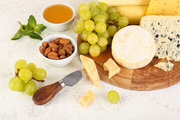 Wooden board with different types of cheese and grapes on light background, closeup