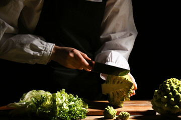 Woman cutting fresh Romanesco broccoli on dark background, closeup