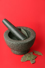 Mortar and pestle with bay leaves on red background