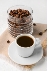 Cup of coffee and jar with beans on light background