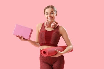 Sporty young woman with mat and block for yoga on pink background