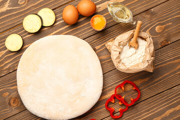 Raw dough and ingredients for preparing vegetable pie on wooden background