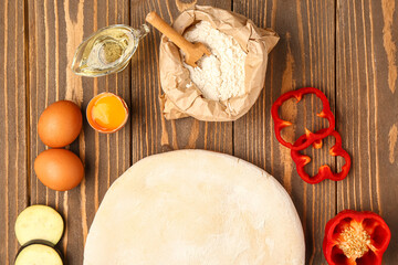 Raw dough and ingredients for preparing vegetable pie on wooden background