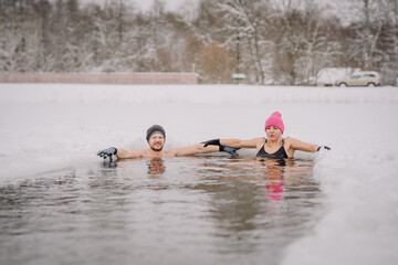Winter swimming. Man and women in frozen lake ice hole. Swimmers wellness in icy water. How to swim in cold water. . white hat and gloves swimming clothes. Nature lake