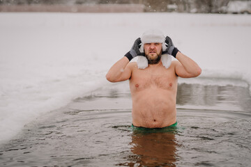 A man with green shorts and a white hat stands in cold water in winter, a healthy lifestyle.