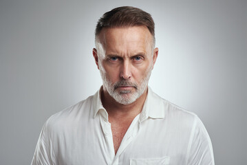 I dont find that funny at all. Studio portrait of a mature man looking angry against a grey...