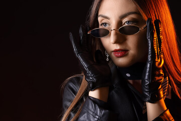 Beautiful young woman in leather gloves and jacket on dark background