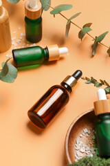 Wooden plate with bottles of cosmetic oil and eucalyptus branch on orange background