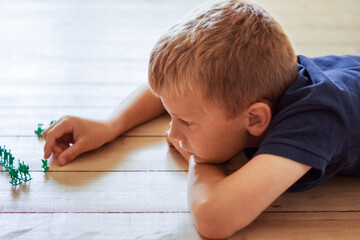 Closeup of a cute blond young boy playing with miniature toy soldiers on floor