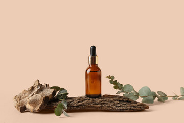 Bottle of cosmetic oil with eucalyptus branches and tree bark on pale pink background