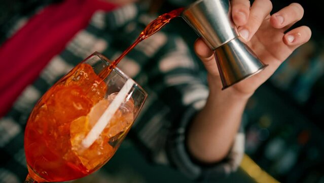 Preparation of Aperol Spritz cocktail bartender pouring prosecco into a glass with ice at the bar close-up