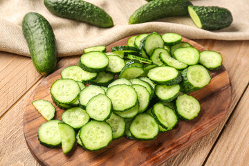 Board with fresh cut cucumbers on wooden background