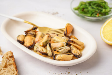 Plate with pickled mussels and bowl of seaweed salad on white background