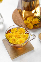 Glass cup of healthy dandelion tea and teapot on white background