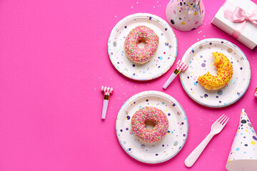 Paper disposable plates with donuts and party blowers on pink background