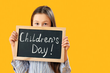 Little girl holding chalkboard with text CHILDREN'S DAY on yellow background