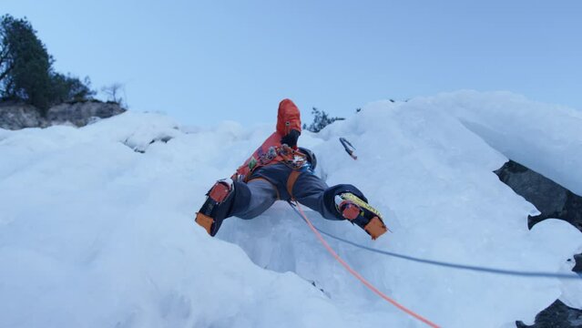 An athlete climbs an icefall with ice axes and crampons in the Alps, Switzerland