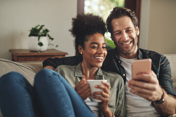 Fototapeta Look at whats trending online today. a happy young couple using a cellphone together while relaxing on a couch at home. obraz