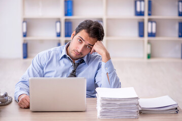 Fototapeta premium Young male employee and too much work at workplace