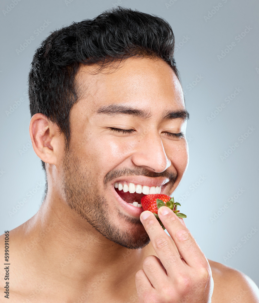 Poster strawberries are simply irresistible. a man taking a bite of a strawberry while standing against a g