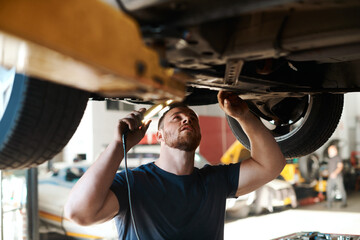 Heres where the problem lies. a mechanic working under a lifted car.