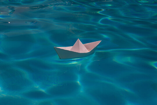 Paper boat sailing on blue water surface. Paper boat into water. Concept of tourism, travel dreams vacation holiday, dreaming traveling, sailing adventure.
