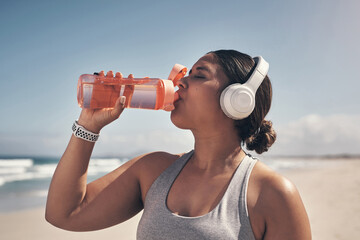 Exercise and drink plenty of water. a woman wearing headphones and drinking water while out for a workout on the beach.