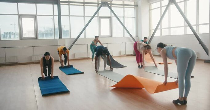 Group of friends prepare sports mats for yoga class in gym