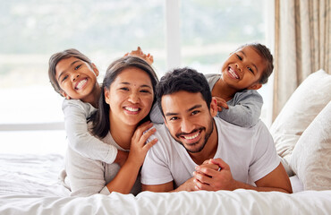 Young happy smiling couple looking cheerful and relaxed while sharing the bed with their daughters....