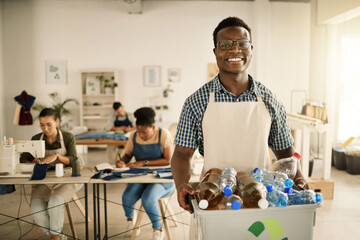 Fototapeta na wymiar African american designer holding a recycling bin. Businessman holding a bucket of recycled plastic bottles. Young tailor holding a recycling bin. Smiling designer recycling plastic bottles