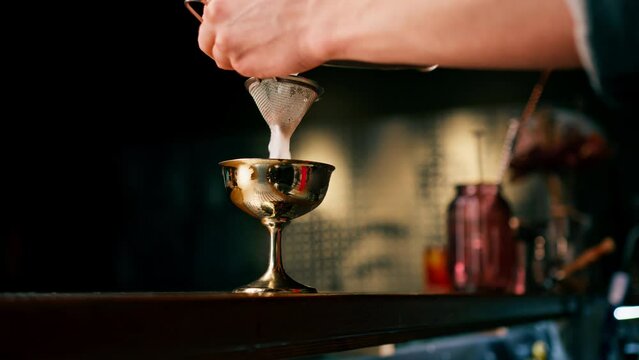The bartender pours the finished cocktail into a beautiful glass from a shaker through an alcohol strainer