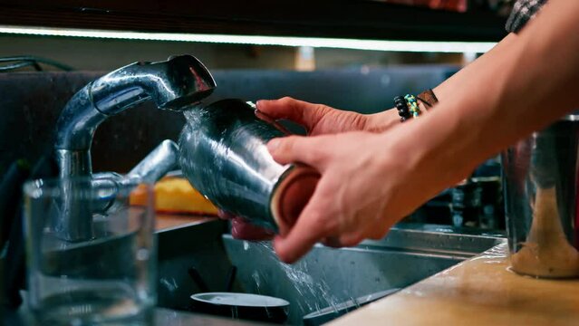 a professional bartender washes a shaker in the sink after making a cocktail after work
