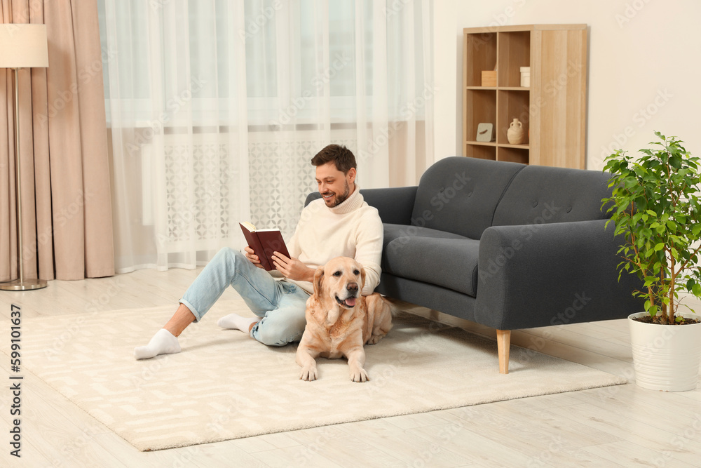 Poster man reading book on floor near his cute labrador retriever at home