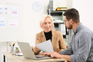 Fototapeta premium Boss and employee with laptop discussing work issues at wooden table in office