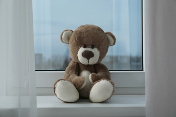 Cute lonely teddy bear on windowsill indoors