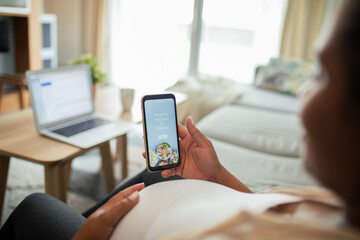 Young pregnant latina woman using a diet app on her smart phone while sitting on a couch in the...