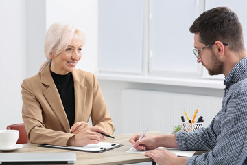 Happy woman having conversation with man at wooden table in office. Manager conducting job interview with applicant