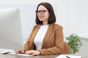 Happy young intern working with computer at table in modern office