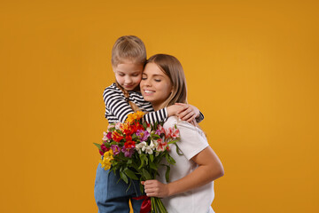 Fototapeta na wymiar Little daughter congratulating her mom with flowers on orange background. Happy Mother's Day