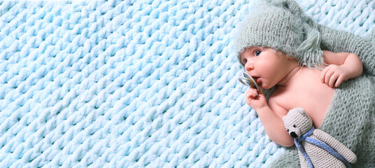 Cute baby baby with pacifier and crochet toy on light blue blanket, top view. Banner design with...