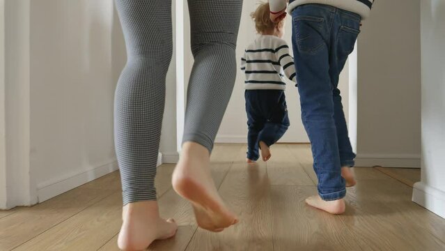 Closeup of mother and two boys running on the wooden floor at home. Concept of family love, joy, and fun in a household.